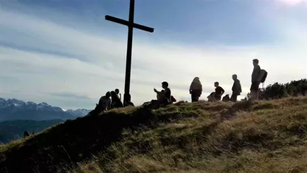 Mitarbeitende machen Pause an einem Gipfelkreuz in den Bergen mit Panorama im Hintergrund